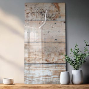 Op de afbeelding: Een rechthoekige wandklok met een houten plankontwerp. De wijzerplaat heeft een heldere glazen overlay met zilverkleurige wijzers en cijfers. De houten achtergrond heeft een natuurlijke, lichtbruine kleur.