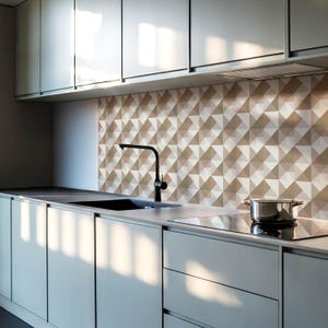 May include: A modern kitchen with grey cabinets and a stainless steel hob. The backsplash is made of white and brown geometric tiles.