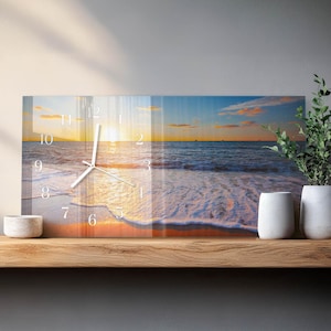 May include: A rectangular wall clock featuring a beach scene with a sunset. The clock face displays white numerals and hands against the backdrop of the ocean, sand, and sky. The colors include shades of orange, yellow, blue, and white.