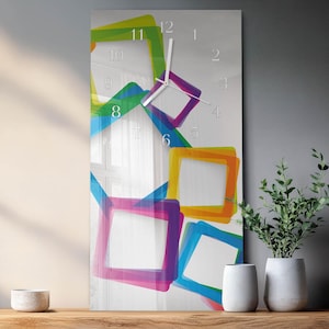 Puede incluir: Un reloj de pared rectangular con esfera blanca y manecillas transparentes. El reloj presenta marcos cuadrados superpuestos y coloridos en tonos rosa, azul, verde y amarillo. El reloj mide aproximadamente 30 cm de ancho y 61 cm de alto.