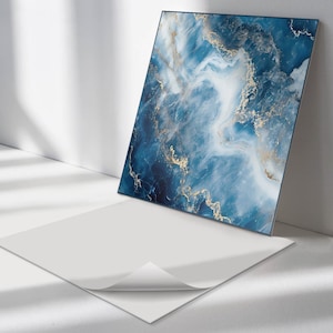 May include: A square, blue and white abstract print with gold accents. The print is on a white background and is framed with a thin black frame.