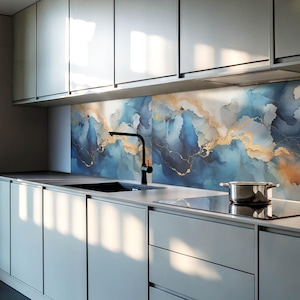 Op de afbeelding: Een moderne keuken met grijze kasten en een achterwand met een abstract ontwerp van blauwe en gouden swirls. Een zwarte kraan is gemonteerd boven een roestvrijstalen gootsteen. Een zwart fornuis is zichtbaar op de voorgrond.