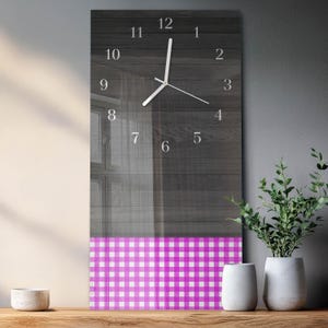 May include: A rectangular wall clock with a dark gray wood-grain background and white numerals. The bottom section features a pink and white checkered pattern. The clock hands are white. The clock is displayed on a wooden surface.