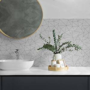 May include: White bathroom sink with a chrome faucet and a round mirror above it. A white ceramic vase with green eucalyptus branches sits on a woven tray with two white bottles and a small wooden frame.
