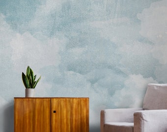 May include: A light blue watercolor-style wall mural with a white wooden cabinet and a potted plant in front of it. A light gray armchair is on the right side of the image.