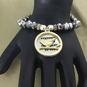 May include: A gold bracelet with a charm that says "Remember I Want To You" with a bird on a branch. The bracelet is made of black and silver beads.