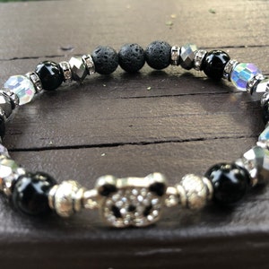 Könnte beinhalten: Schwarzes und silbernes Perlenarmband mit einem Pandabande. Das Armband besteht aus schwarzen Lavasteinen, schwarzen Onyxperlen, klaren Kristallperlen und silbernen Abstandshaltern.