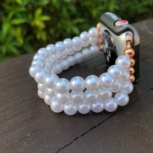May include: A white pearl watch band with a silver and rose gold Apple Watch.