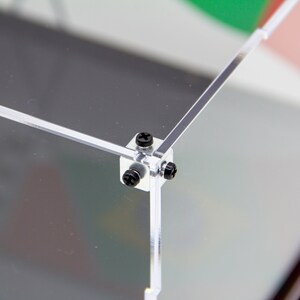 May include: Close-up of a clear acrylic display case with black screws securing the corners.