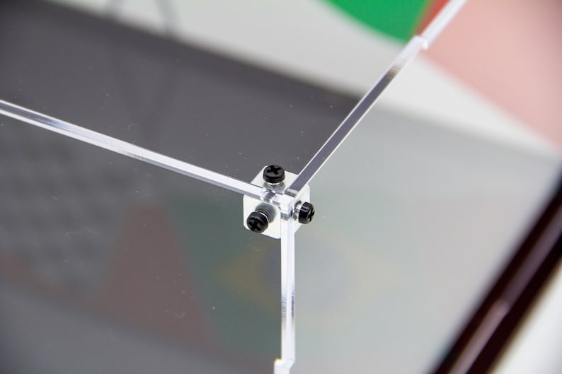 May include: Close-up of a clear acrylic display case with black screws securing the corners.