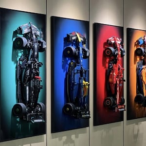 Peut inclure: Quatre œuvres d'art encadrées représentant des voitures de course de Formule 1 construites avec des blocs de construction noirs, bleus, rouges et oranges. Chaque voiture est montée sur un fond coloré : turquoise, bleu, rouge et orange. Les œuvres sont exposées sur un mur neutre.