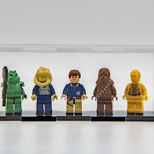 May include: Five Star Wars Lego minifigures in a clear display case. The minifigures are from left to right: a green and brown creature, a yellow and blue figure, a blue and brown figure, a brown figure, and a gold figure.