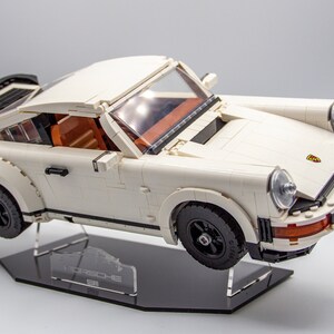 May include: A white Lego Porsche 911 Turbo model on a black display stand with the word "Porsche" printed on it.