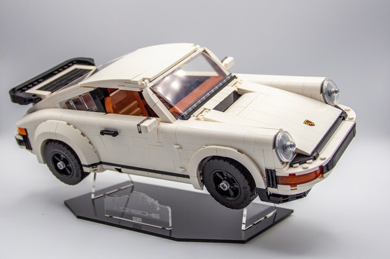 May include: A white Lego Porsche 911 Turbo model on a black display stand with the word "Porsche" printed on it.