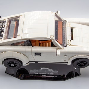 May include: A white Lego Porsche 911 Turbo model with black accents and a clear windscreen. The model is displayed on a black display stand with the word "Porsche" printed on it.