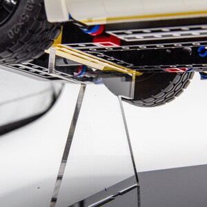 May include: A white Lego vehicle with black tyres and a yellow stripe on the bottom. The vehicle is on a clear acrylic display stand.