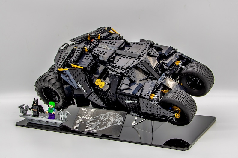 May include: A black LEGO The Dark Knight Tumbler set with Batman and The Joker minifigures. The Tumbler is displayed on a black stand with a printed description of the vehicle.