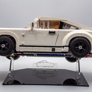 May include: A white Lego Porsche 911 Turbo model on a black display stand. The car is on a clear acrylic stand with a Porsche logo.