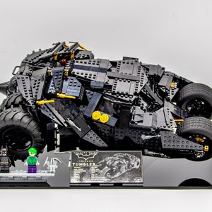 May include: A black LEGO The Dark Knight Tumbler model with a black and gold display stand. The model includes two minifigures: Batman and The Joker.