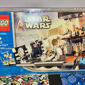 May include: A LEGO Star Wars Cloud City set, featuring a blue and white box with the LEGO logo and the words "Star Wars" in white. The box shows a detailed model of Cloud City, with characters from the Star Wars franchise, including Lando Calrissian, Boba Fett, and Princess Leia. The set includes 698 pieces and is recommended for ages 9 and up.
