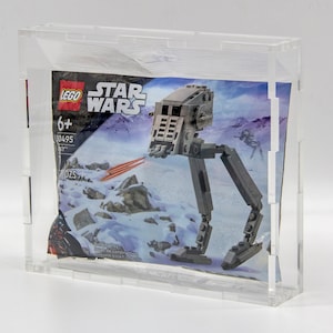 May include: A clear acrylic display case with a LEGO Star Wars AT-ST walker minifigure inside. The minifigure is gray and has red laser beams. The packaging shows the text "LEGO Star Wars" and "6+".