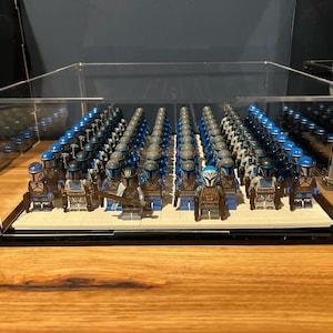 May include: A display case filled with a collection of blue and gray Lego minifigures. The minifigures are arranged in rows and columns, and they are all wearing helmets and armor. The case is made of clear plastic and has a black base.