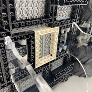 May include: Close-up of a black and gray Lego model with a white frame. The model has a detailed interior and a large tire on the right side.