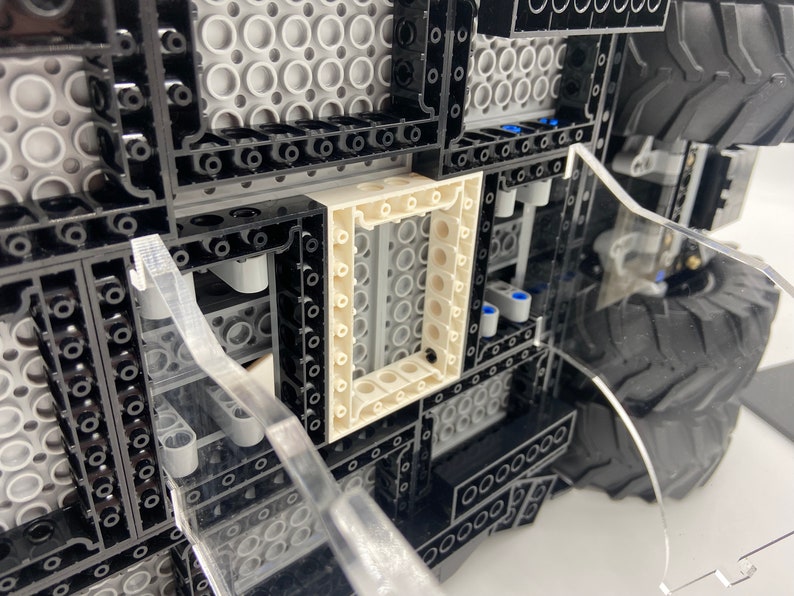 May include: Close-up of a black and gray Lego model with a white frame. The model has a detailed interior and a large tire on the right side.