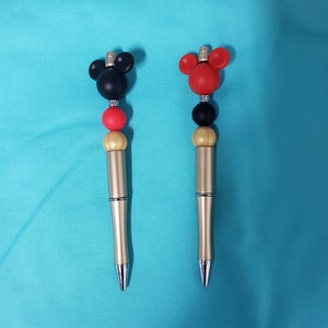 May include: Two gold pens with black and red Mickey Mouse heads on top. The pens have gold and red beads on the shaft.