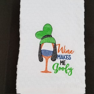May include: White kitchen towel with an embroidered design of a wine glass with a Goofy-like face and the text "Wine Makes Me Goofy".