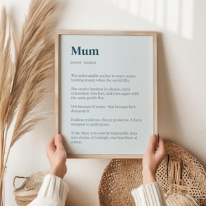 Op de afbeelding: Een ingelijste print met het woord "Mum" bovenaan, gevolgd door een definitie en een gedicht. De print wordt door handen vastgehouden en heeft een lichtblauwe achtergrond met donkerblauwe tekst. De lijst heeft een lichte houtkleur.