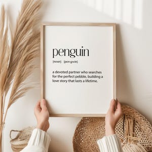 May include: A framed print with a minimalist design featuring the word "penguin" and its definition: "a devoted partner who searches for the perfect pebble, building a love story that lasts a lifetime."