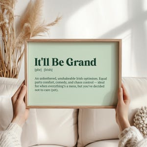 May include: A framed print with the phrase "It'll Be Grand" in dark green lettering. The print has a light green background and a wooden frame. The text below defines the phrase as Irish optimism.