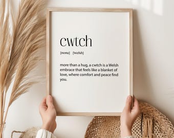 Puede incluir: Una impresión enmarcada con la palabra "cwtch" en texto negro sobre un fondo blanco. La definición de la palabra está debajo en texto negro: "[sustantivo] [galés] más que un abrazo, un cwtch es un abrazo galés que se siente como una manta de amor, donde la comodidad y la paz te encuentran."
