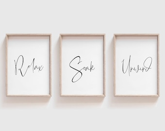 May include: Three framed prints with the words "Relax", "Soak", and "Unwind" written in a cursive font. The frames are light brown wood and the prints are on white paper.