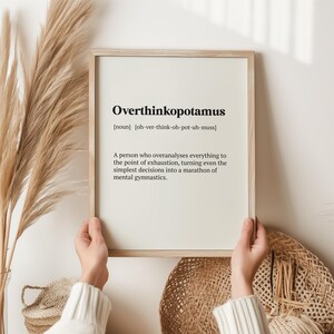 May include: A framed print with a white background and black text defining the word "Overthinkopotamus" as a noun, meaning "a person who overanalyses everything to the point of exhaustion, turning even the simplest decisions into a marathon of mental gymnastics."