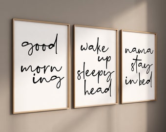 Op de afbeelding: Drie ingelijste prints met zwarte kalligrafie op een witte achtergrond. De eerste print zegt "good morning", de tweede print zegt "wake up sleepy head" en de derde print zegt "mama stay in bed".