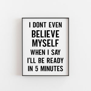 Op de afbeelding: Zwart-wit typografieprint met de tekst "Ik geloof mezelf niet eens als ik zeg dat ik over 5 minuten klaar ben". De print is ingelijst in een zwart frame.