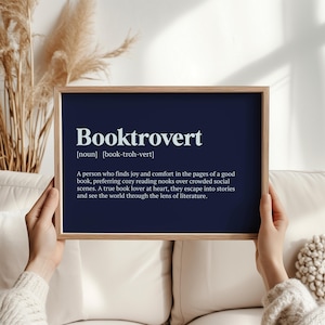 May include: A navy blue printable wall art print with the definition of the word "Booktrovert" in white text. The definition reads: "A person who finds joy and comfort in the pages of a good book, preferring cozy reading nooks over crowded social scenes. A true book lover at heart, they escape into stories and see the world through the lens of literature."