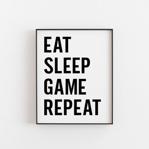 May include: Black and white framed print with the text "EAT SLEEP GAME REPEAT" in bold letters.
