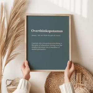 May include: A teal framed print with the word "Overthinkopotamus" defined as "a person who overanalyses everything to the point of exhaustion, turning even the simplest decisions into a marathon of mental gymnastics."