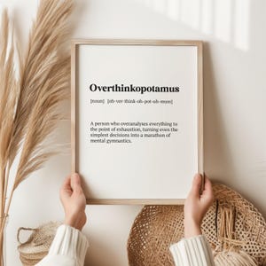 May include: A framed print with a white background and black text defining the word "Overthinkopotamus" as a noun, meaning "a person who overanalyses everything to the point of exhaustion, turning even the simplest decisions into a marathon of mental gymnastics."