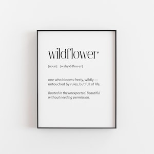 May include: A framed print with the word "wildflower" in a bold, elegant font. The definition below describes a wildflower as blooming freely, untouched by rules, and full of life. The print is in a black frame.