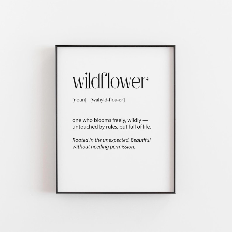 May include: A framed print with the word "wildflower" in a bold, elegant font. The definition below describes a wildflower as blooming freely, untouched by rules, and full of life. The print is in a black frame.