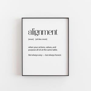May include: A framed print featuring the word "alignment" in a bold, sans-serif font. The definition is provided below, stating "when your actions, values, and purpose all sit at the same table." The text is in black on a white background.
