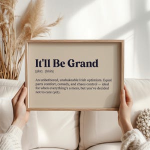May include: A framed print featuring the phrase "It'll Be Grand" in dark blue. The print has a beige background and a definition of the phrase, highlighting Irish optimism and a sense of comfort.