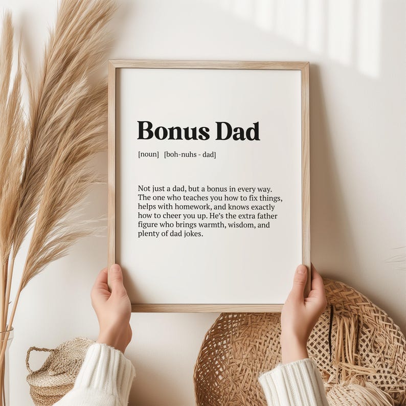 May include: A printable wall art print with a black and white definition of "Bonus Dad" with the pronunciation "boh-nuhs - dad". The definition reads "Not just a dad, but a bonus in every way. The one who teaches you how to fix things, helps with homework, and knows exactly how to cheer you up. He's the extra father figure who brings warmth, wisdom, and plenty of dad jokes."