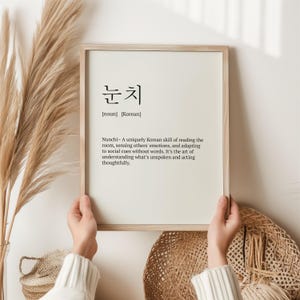 May include: A framed print with the Korean word "눈치" (nunchi) and its definition. Nunchi is a uniquely Korean skill of reading the room, sensing others' emotions, and adapting to social cues without words. It's the art of understanding what's unspoken and acting thoughtfully.