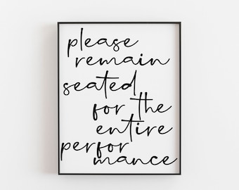 May include: A framed print with the text "please remain seated for the entire performance" in a black, handwritten-style font. The print has a white background and a black frame, suitable for bathroom decor.