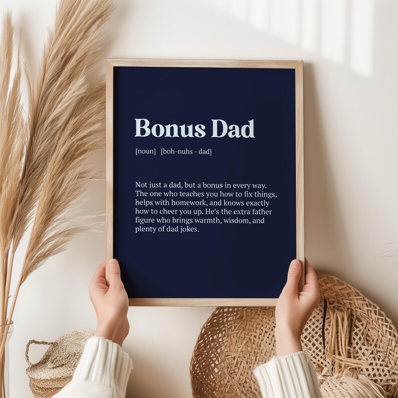 May include: A framed print with a navy blue background and white text that reads "Bonus Dad [noun] [boh-nuhs - dad] Not just a dad, but a bonus in every way. The one who teaches you how to fix things, helps with homework, and knows exactly how to cheer you up. He's the extra father figure who brings warmth, wisdom, and plenty of dad jokes."